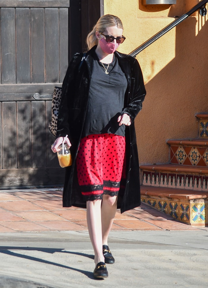 Pregnant Emma Roberts wears a black T-shirt with a red polka-dot midi skirt and long black velvet coat in Los Angeles