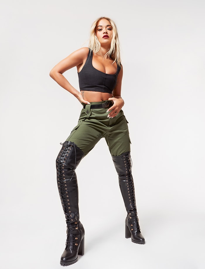 Rita Ora strikes a powerful pose in her ShoeDazzle collection, grounding the utilitarian look with black lace-up thigh-high boots featuring chunky block heels and gold-tone hardware