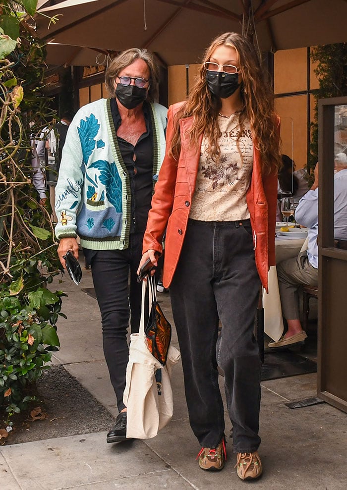 Bella Hadid gives relaxed family-lunch dressing a streetwear edge in an oversized coral leather jacket, printed cream top, slouchy black jeans, and chunky New Balance x Stray Rats sneakers