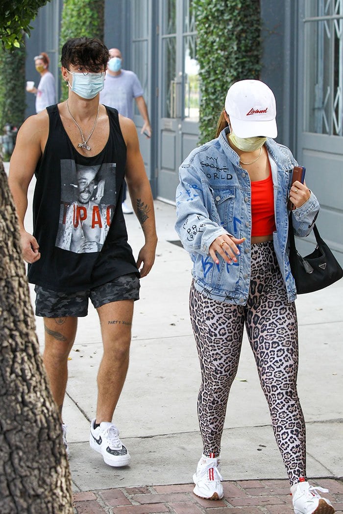Addison Rae heads to a workout session in Los Angeles on November 3, 2020, pairing Aries x New Balance 327 sneakers with Onzie leopard-print leggings, a Stax red crop top, and a customized denim jacket, while Bryce Hall follows in Louis Vuitton-inspired Nike Air Force 1 sneakers