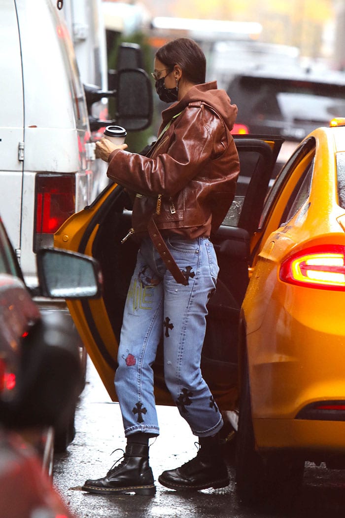 Irina Shayk bundles up in a brown leather jacket with a brown hooded sweater and Chrome Hearts jeans