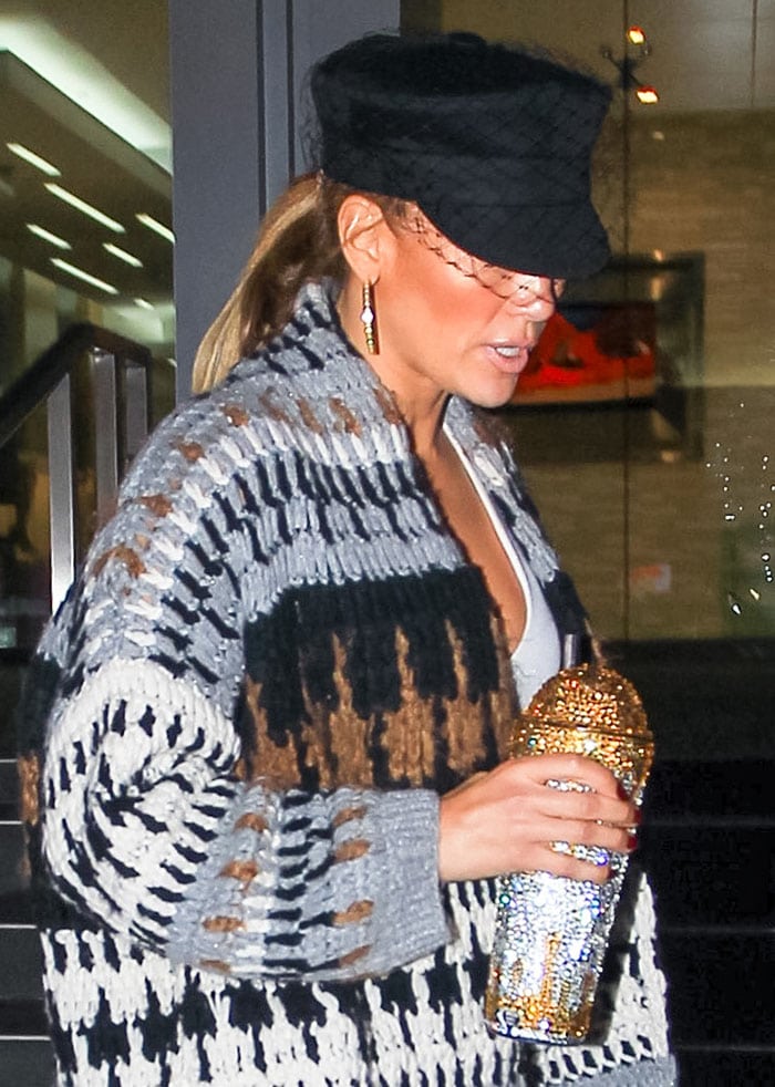 Jennifer Lopez wears bronzer and a nude lip shade, topping off her look with a Dior newsboy cap and carrying a sparkling TaylorMadeBling gold-drip tumbler