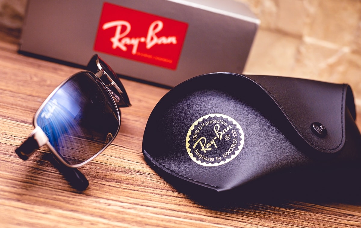 A pair of Ray-Ban sunglasses is displayed alongside the brand’s signature protective case and packaging box, highlighting the premium accessories that accompany an authentic purchase