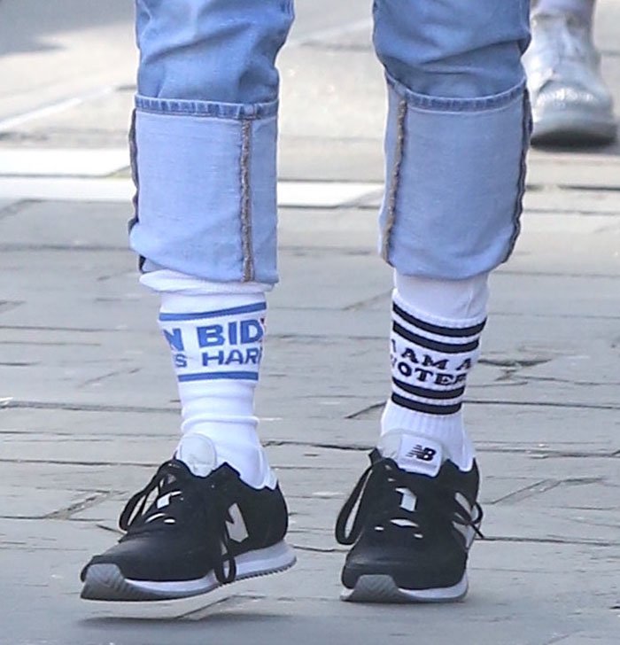 Sarah Jessica Parker adds a playful political twist to her casual New York City outfit, cuffing her light-wash mom jeans to reveal mismatched “I Am a Voter” and “Biden Harris” statement socks paired with classic black New Balance sneakers