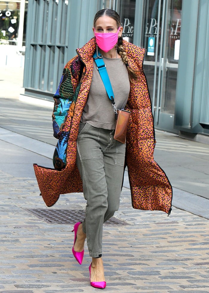 Sarah Jessica Parker brightens a gray November day while visiting her Seaport shoe store in New York City on November 19, 2020, pairing a bold Farm Rio jungle-print puffer coat and cuffed khaki jeans with hot pink SJP “Rampling” pumps and a matching neon face mask