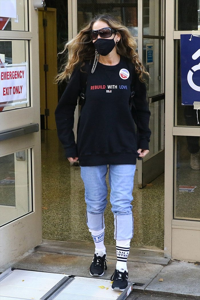 Sarah Jessica Parker exits a New York City polling place in a Jason Wu “Rebuild With Love” sweatshirt, cuffed light-wash mom jeans, mismatched political statement socks, and black New Balance sneakers, blending civic pride with her signature effortless Manhattan street style