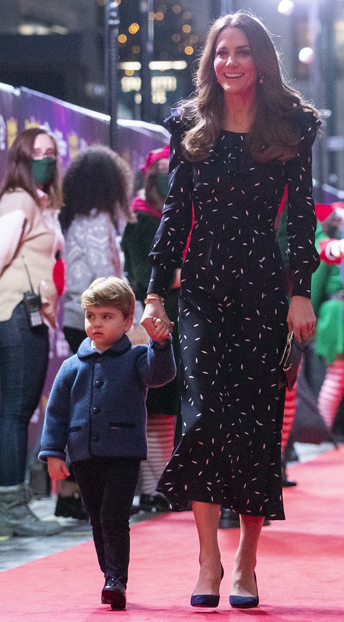 Kate Middleton holds Prince Louis’ hand on the red carpet in a navy Alessandra Rich petal-print midi dress and navy suede Prada pointed-toe pumps