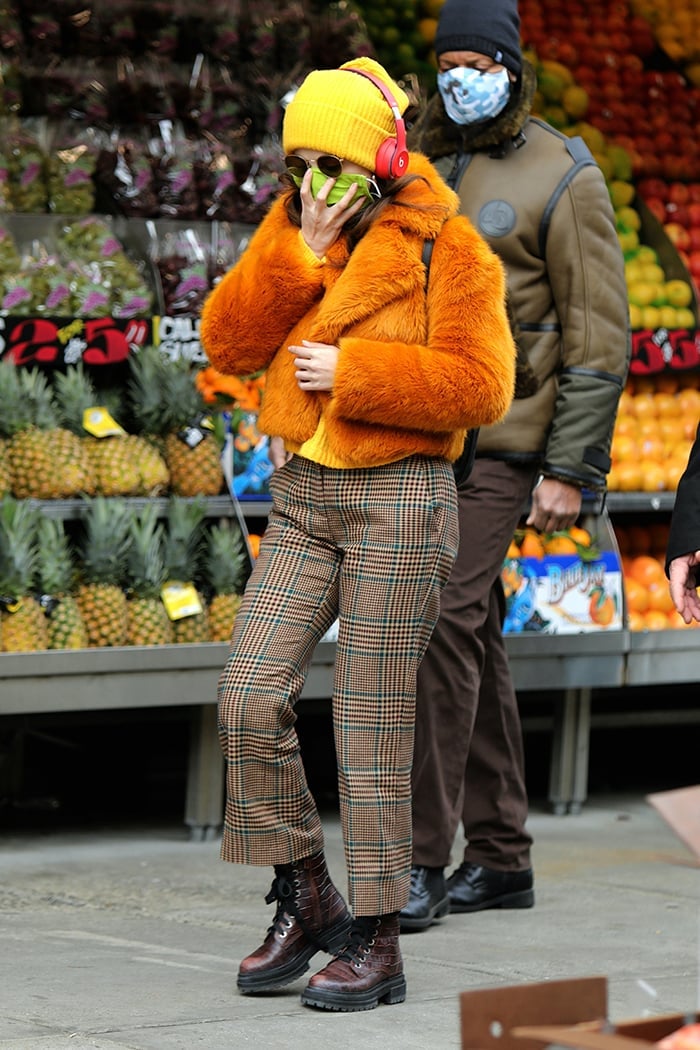Selena Gomez brings a burst of retro fall energy in a burnt-orange Michael Kors faux-fur cropped jacket, yellow knit top, and Veronica Beard plaid slacks, styled with a beanie, red headphones, and chunky Kurt Geiger combat boots while filming “Only Murders in the Building” in New York City on December 7, 2020
