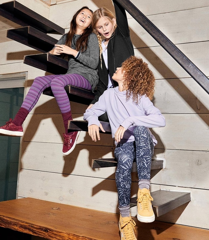 Three friends lounge on a staircase in Lululemon leggings, highlighting the shift toward soft, performance-driven styles that are replacing traditional denim for everyday wear