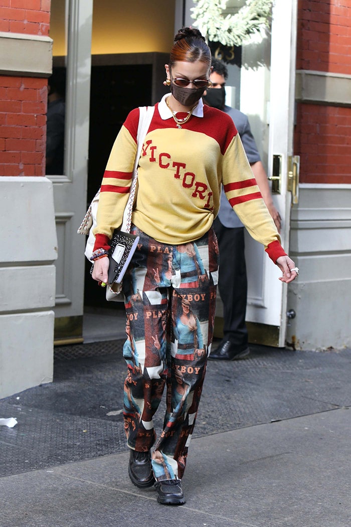 Bella Hadid leans into a ’90s collegiate aesthetic in a red-and-yellow Bode Victoria sweater, styling it with Playboy-print Soulland pants and chunky black lug-sole sneakers
