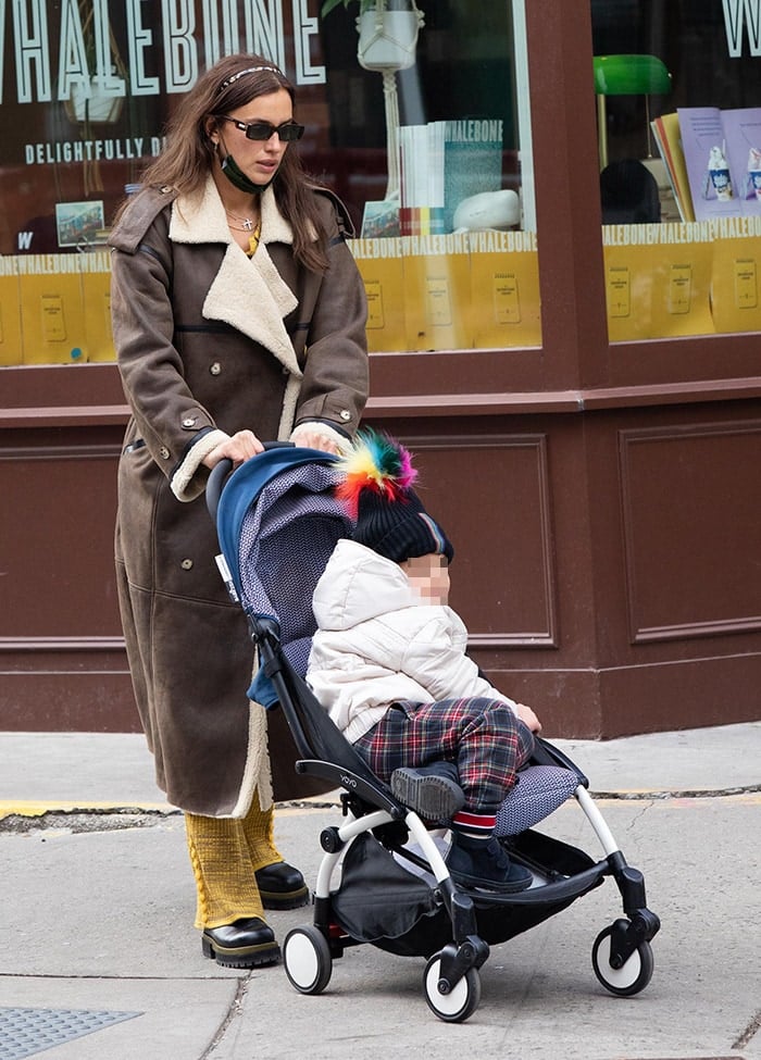 Pushing a stroller along a city sidewalk, she layers warm neutrals and saturated tones, with lug-sole Chelsea boots anchoring the outfit in practicality and urban edge