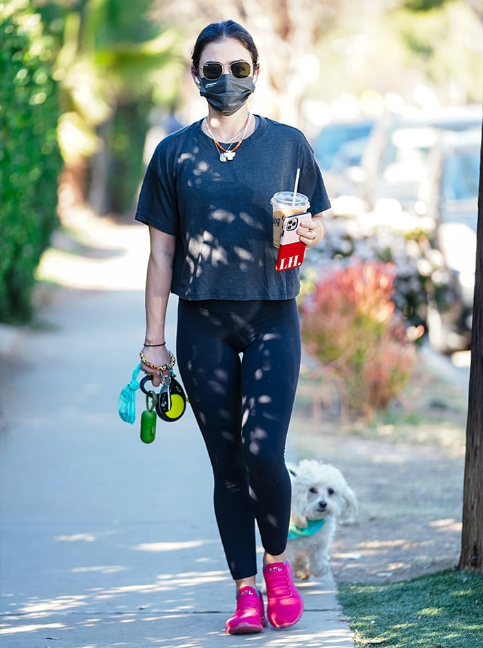 Lucy Hale showcases effortless athleisure in a cropped charcoal tee, black leggings, and bold hot pink APL sneakers while strolling with her dog Elvis