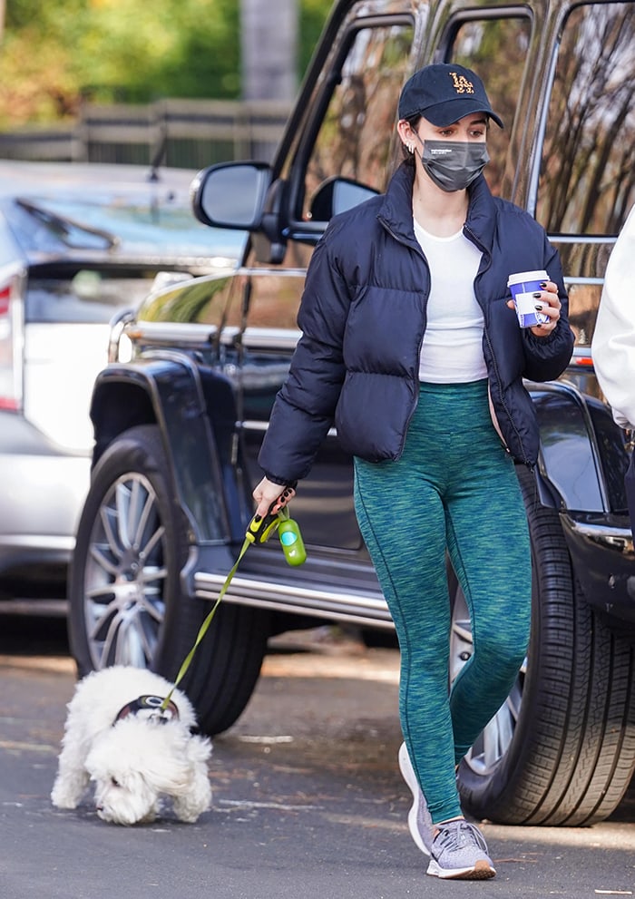 Lucy Hale pairs green leggings with gray Nike Air Zoom Pegasus 36 sneakers, a navy puffer, and an LA baseball cap while walking her dog in Los Angeles