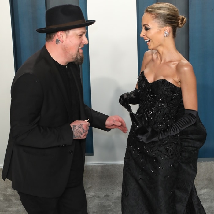 Nicole Richie stuns in a strapless black embellished gown paired with long black gloves at the Vanity Fair Oscar Party, sharing a lighthearted moment with her husband, Joel Madden
