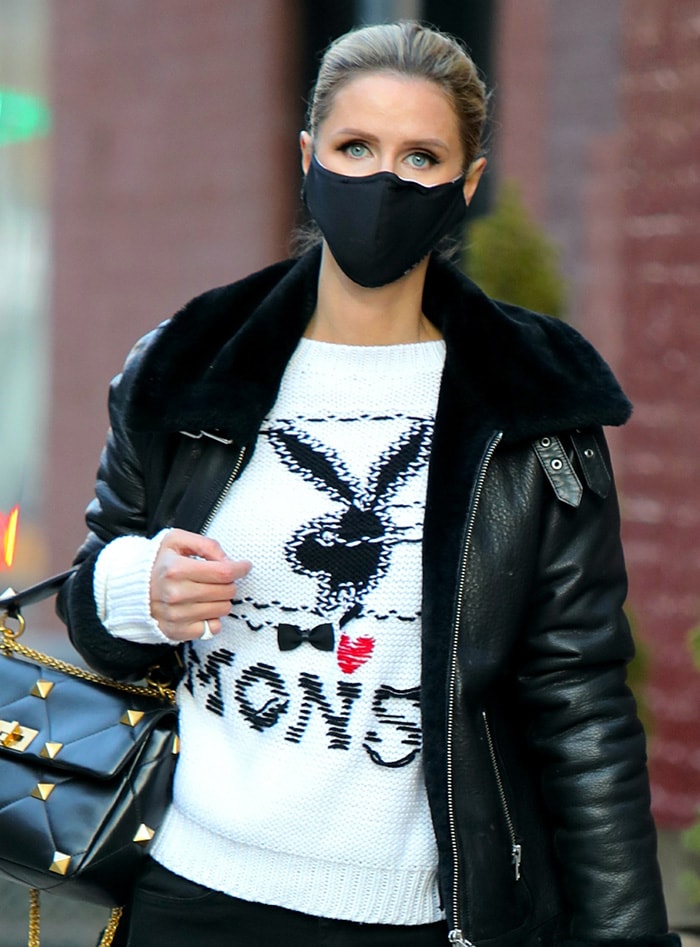 A close-up highlights Nicky Hilton's slicked-back hairstyle, smoky eye makeup, and Monse x Playboy sweater layered beneath her black shearling-collar Muubaa biker jacket