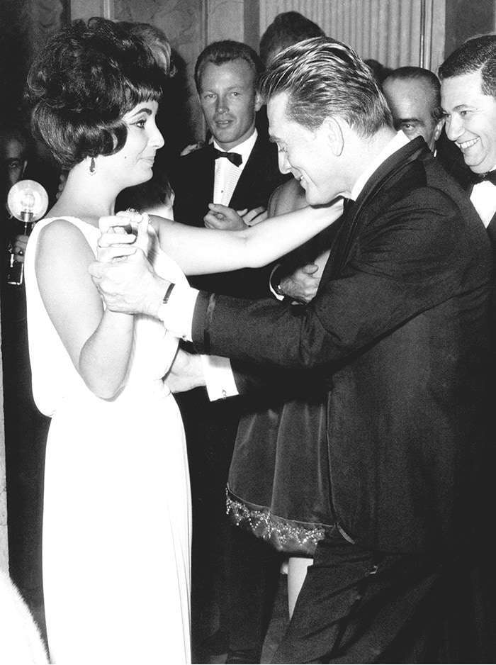 Elizabeth Taylor dances with Kirk Douglas at the Spartacus premiere after-party in Rome in 1961, capturing the jet-set glamour that helped define Valentino’s early couture era