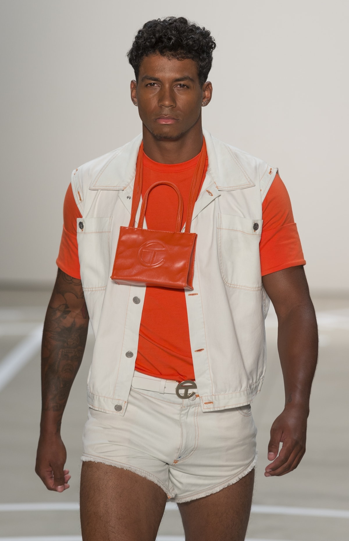A male model walks the runway for Telfar by Telfar Clemens with a TC logo shopping bag