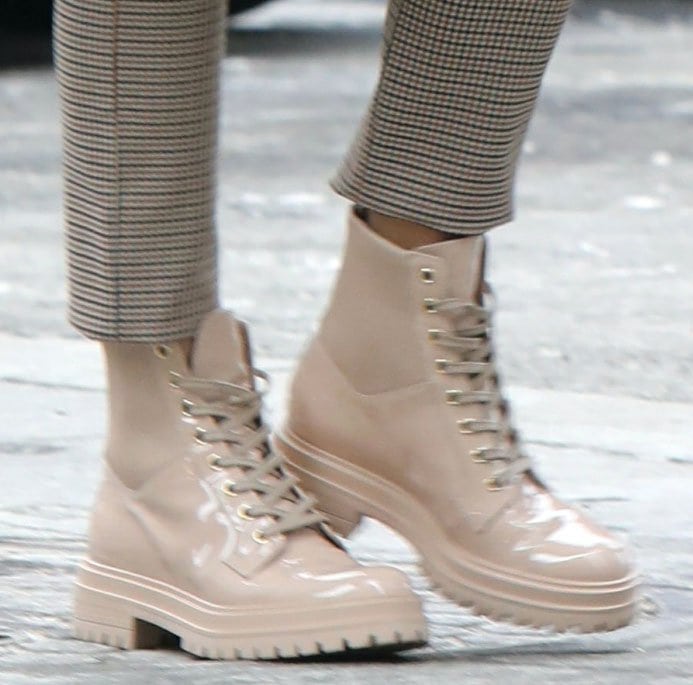 A close-up of Olivia Palermo's beige Gianvito Rossi "Martis" patent combat boots highlights their glossy finish, ribbed stretch panels, lace-up front, and chunky lug soles beneath cropped checkered trousers