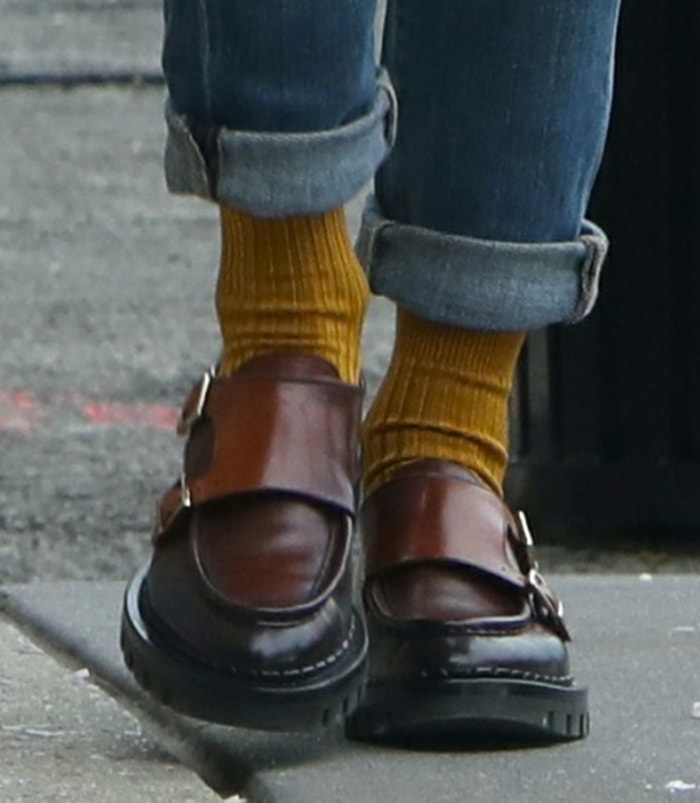 A close-up of Olivia Palermo's chunky Santoni double-monk loafers highlights their rich brown leather, silver buckle straps, and lug soles, with mustard ribbed socks adding a bold pop of color beneath rolled-cuff jeans