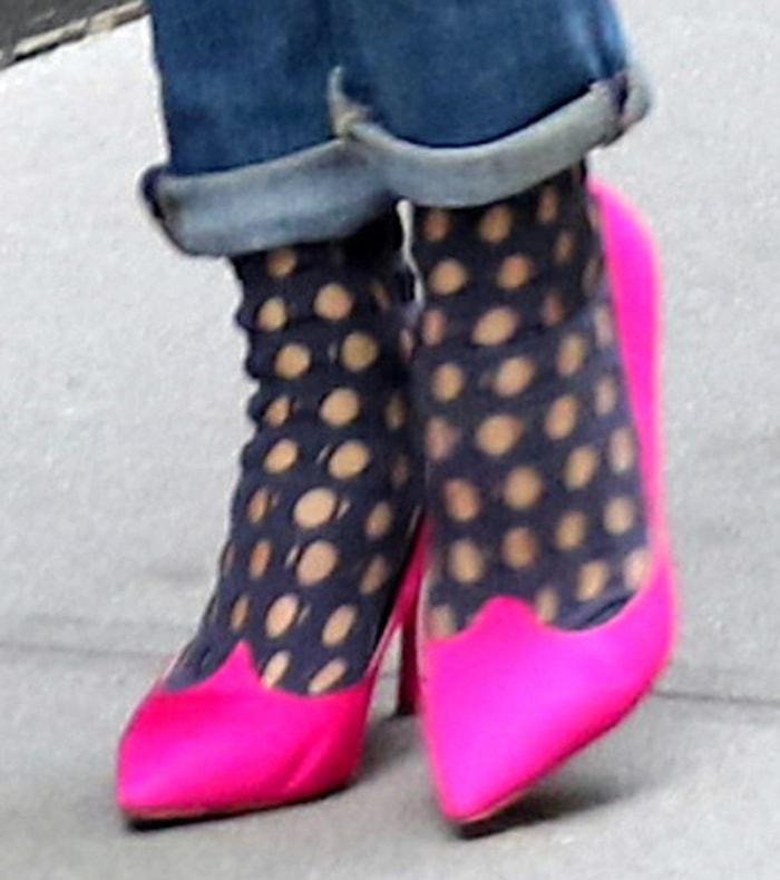 A close-up of Olivia Palermo's hot pink Roger Vivier "Love Vivi" satin pumps showcases their sculptural curved heels and pointed toes, styled with sheer black polka-dot socks beneath rolled-cuff jeans