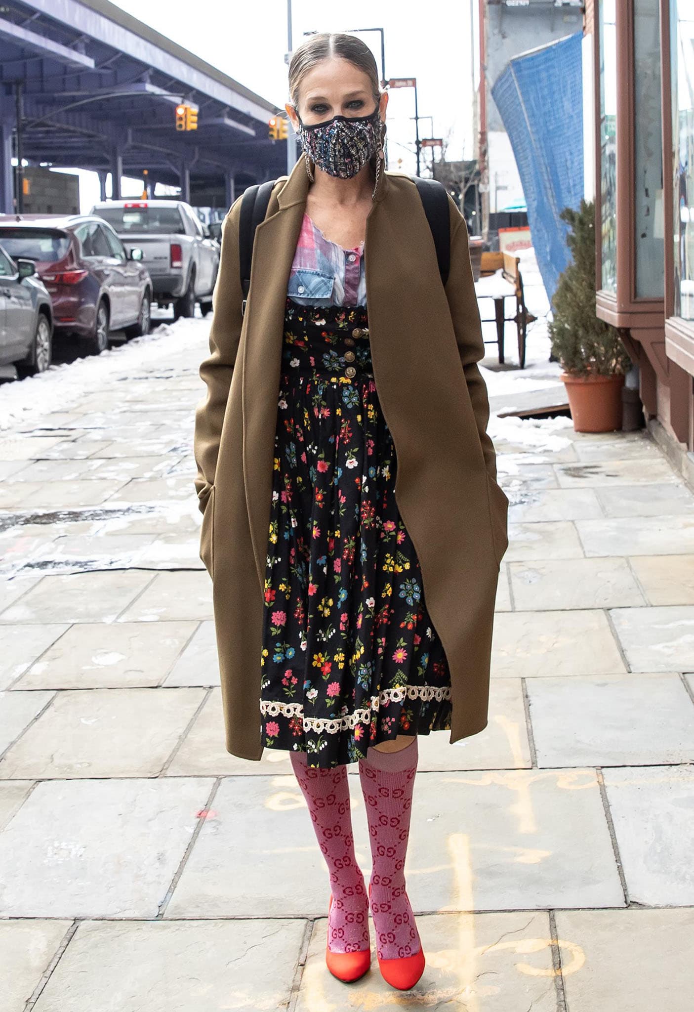 Sarah Jessica Parker layers a camel coat over her floral-and-plaid look, pairing pink Gucci Lamé GG knee-high socks with bright red SJP Fawn pumps outside her South Street Seaport shoe store