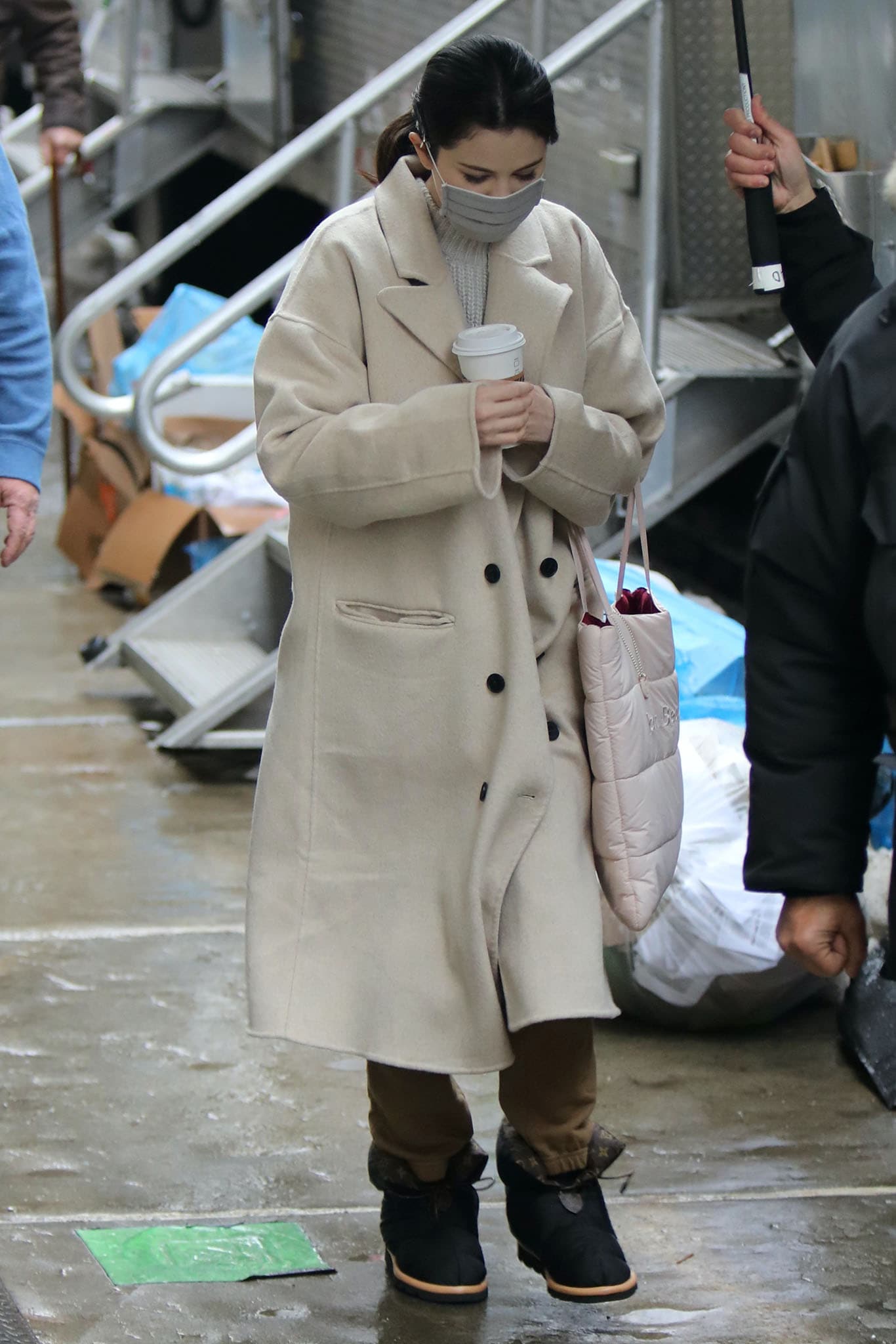 Selena Gomez keeps warm on the New York City set of Only Murders in the Building on February 9, 2021, layering a sand-colored Free People wool coat over cozy fleece joggers and finishing the look with Louis Vuitton Pillow ankle boots