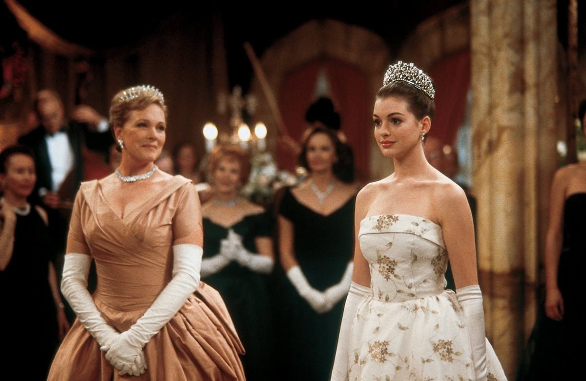 Anne Hathaway, just 18, radiates youthful poise in her breakout role as Mia Thermopolis, standing regally beside Julie Andrews’ graceful Queen Clarisse Renaldi, 65, in this unforgettable ballroom scene from The Princess Diaries