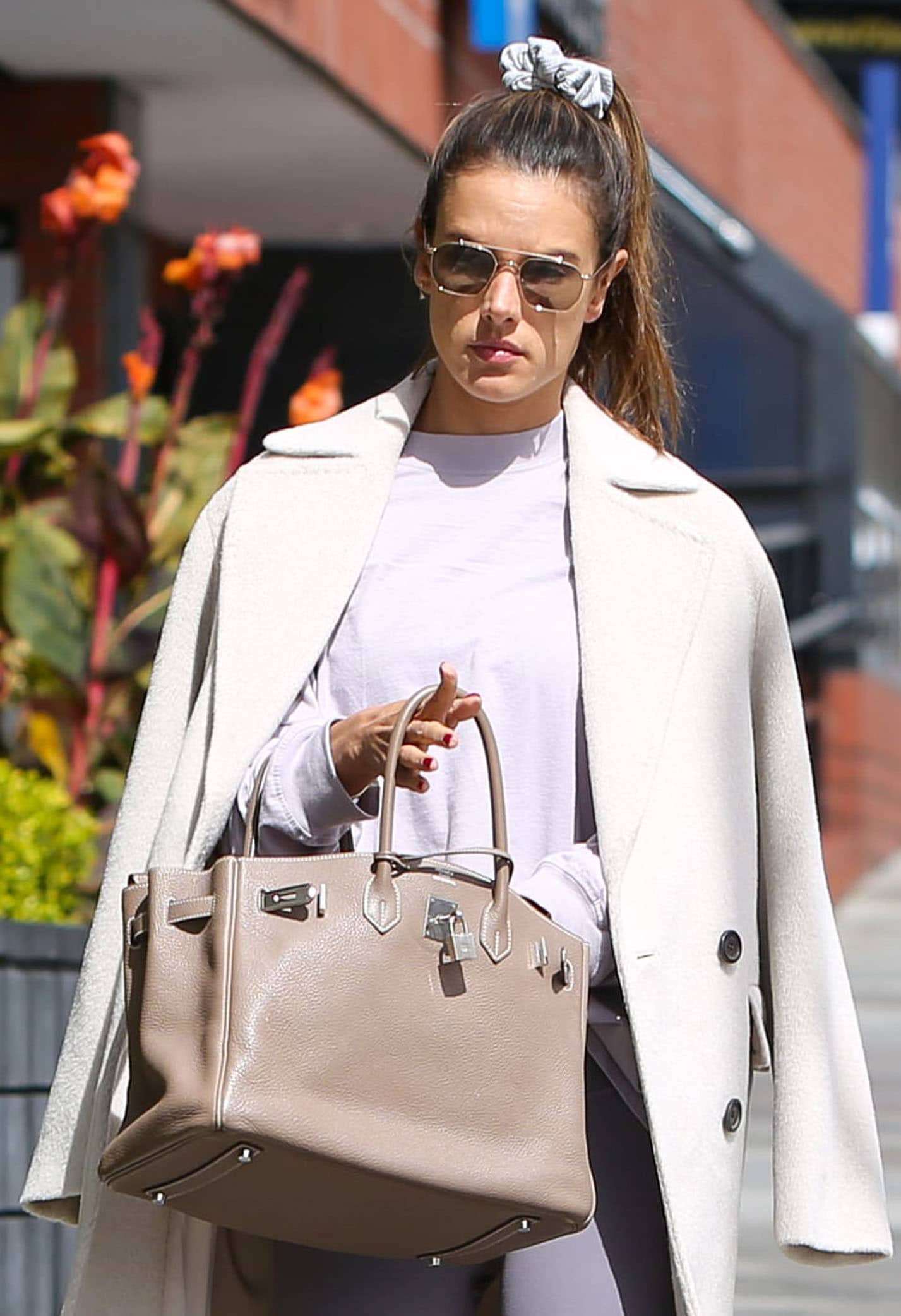 Alessandra Ambrosio carries a 35cm Etoupe Hermès Birkin with her purple-dusk Alo Yoga set and white coat, finishing her Pilates look with Vehla sunglasses and a gray scrunchie