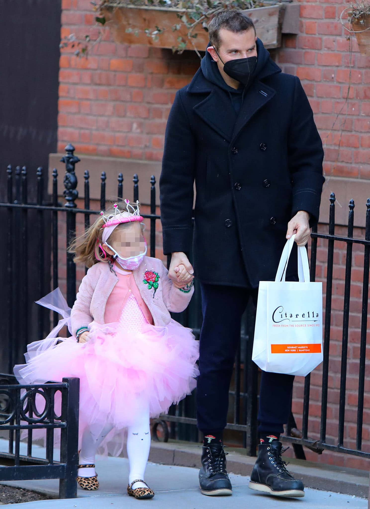 Bradley Cooper keeps his school-run look understated in a black pea coat, navy joggers, and leather high-top shoes while walking hand-in-hand with Lea in her birthday tutu