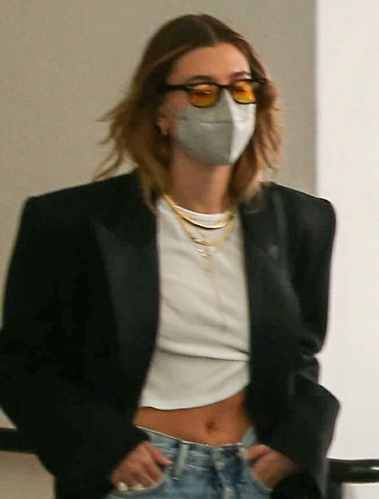 Layered gold necklaces, amber-tinted sunglasses, and strong shoulder tailoring give Hailey Bieber's off-duty look a fashion-forward edge