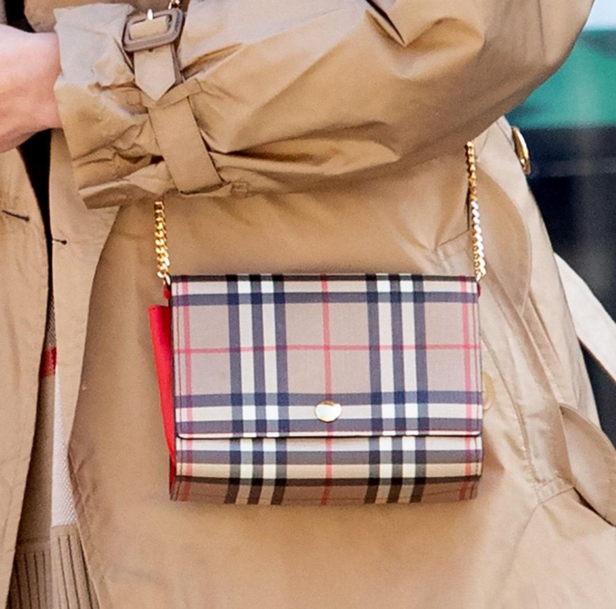 A close-up of Irina Shayk’s Burberry checked leather wallet highlights the heritage pattern and gold chain strap against her tan trench