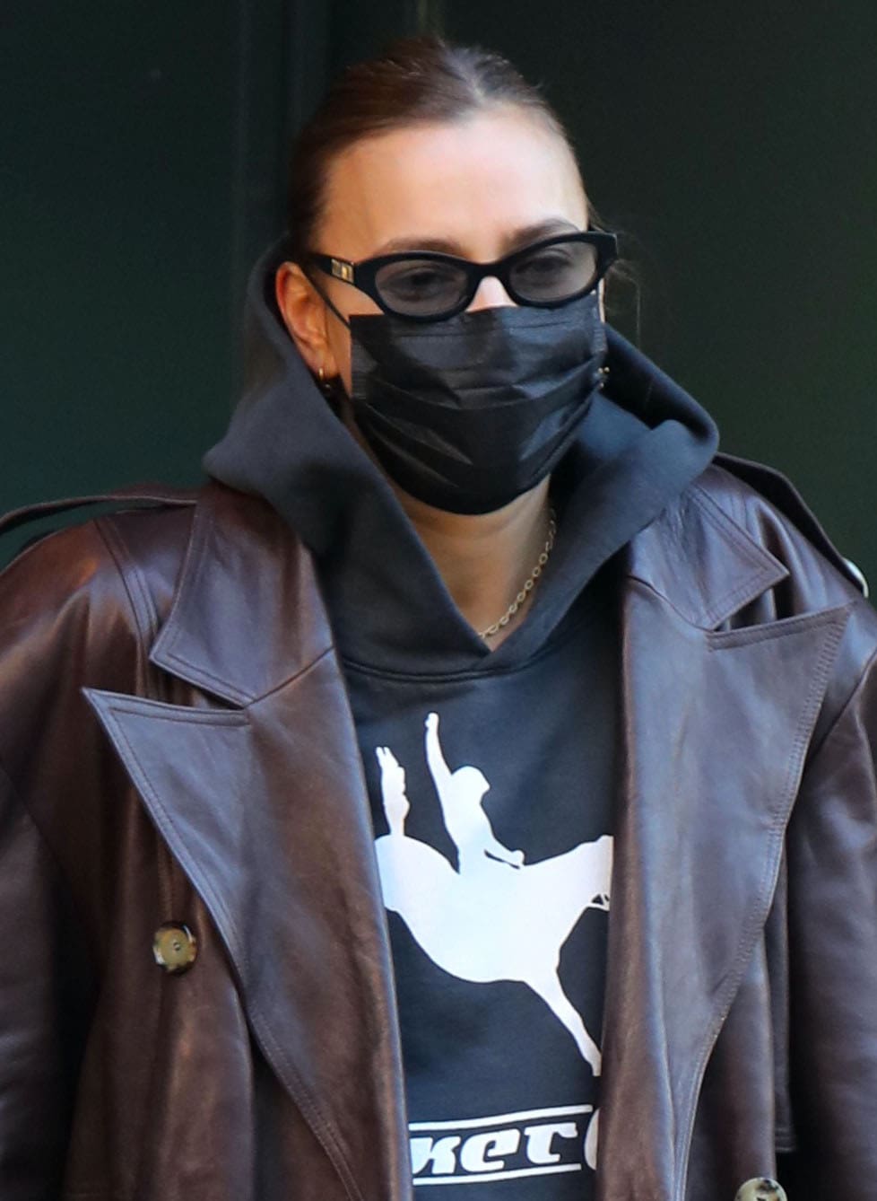 Irina Shayk layers a Bordeaux Magda Butrym leather coat over a black Basket Case Gallery hoodie, accessorizing with Poppy Lissiman “Courtney” sunglasses and a black face mask