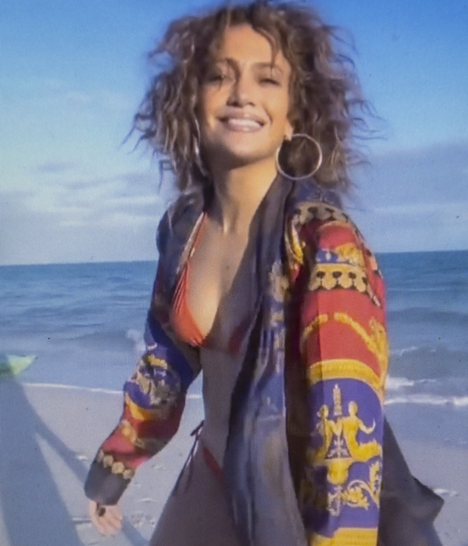Jennifer Lopez beams on the beach in a red bikini and printed cover-up, embracing the sun-soaked glamour that defined her early-2000s style era