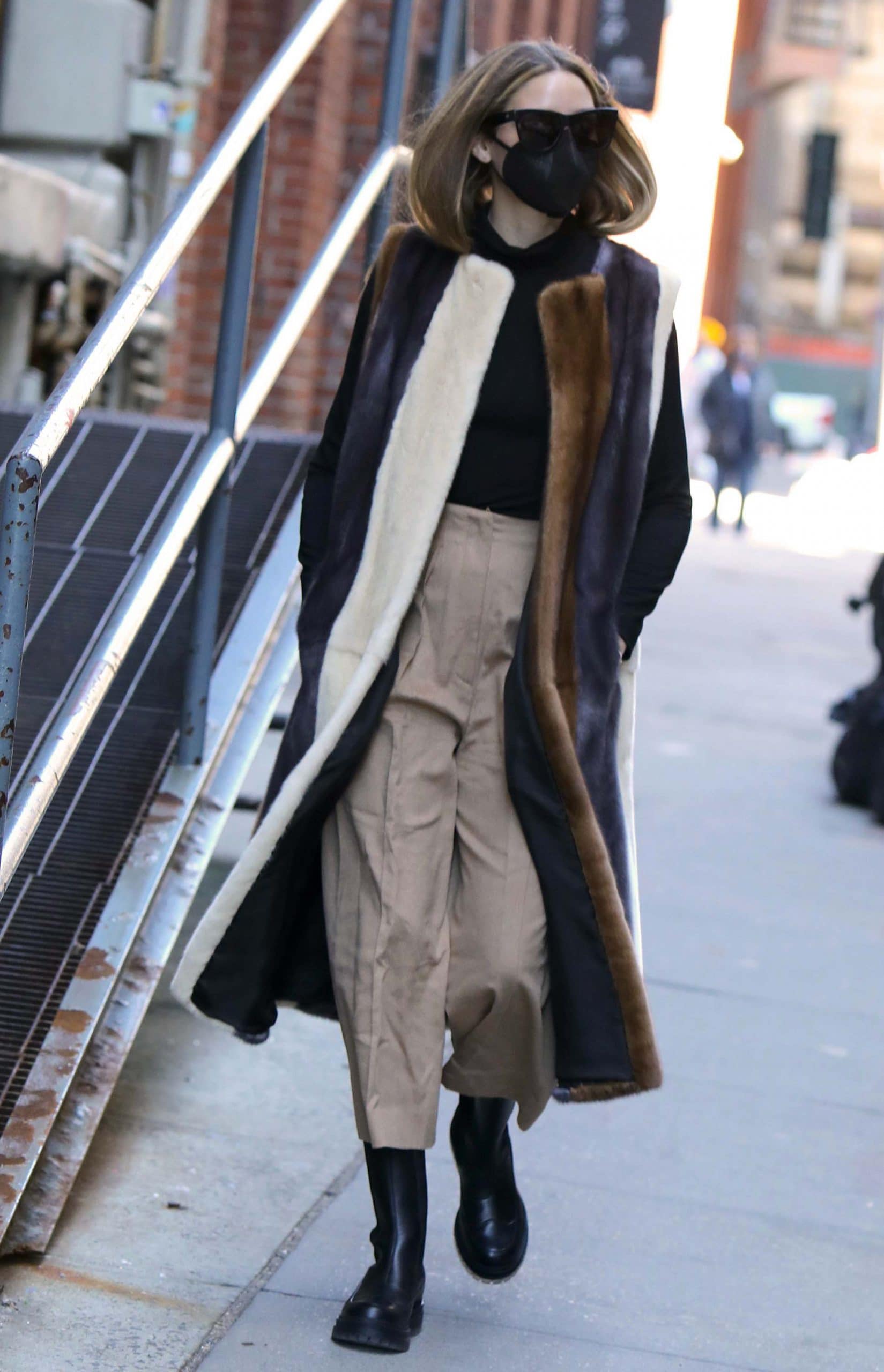 Olivia Palermo effortlessly layers a Pologeorgis faux fur striped vest over a black turtleneck and khaki cropped pants, finishing her winter street style with sleek black Chelsea boots