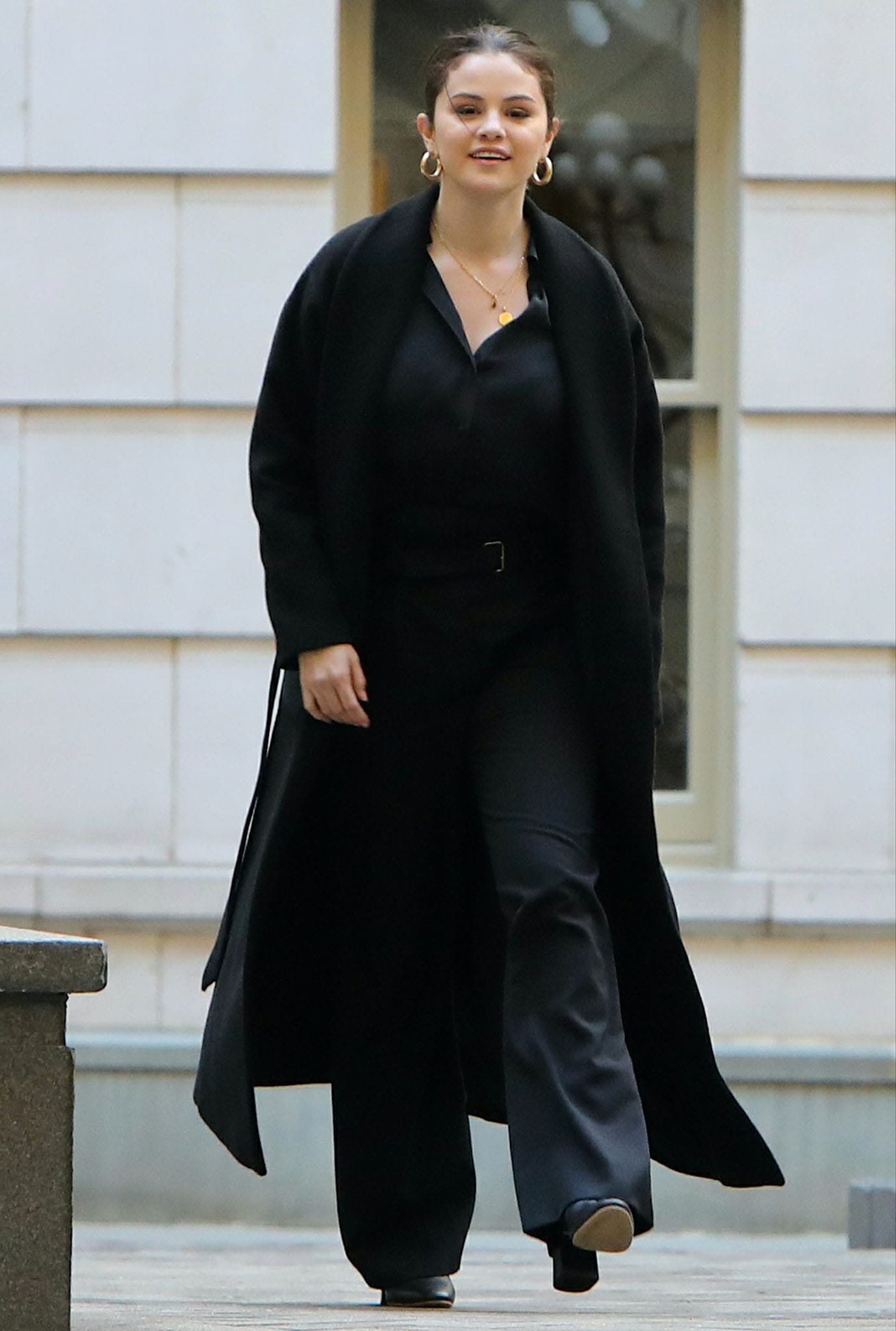 Selena Gomez steps out in a sleek monochrome look, layering a long black coat over a silky blouse and high-waisted trousers, finished with classic block-heeled pumps while filming Only Murders in the Building in New York City