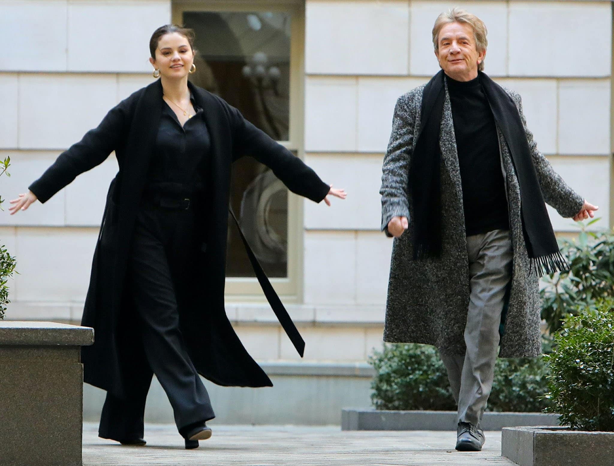 Selena Gomez strides alongside Martin Short while filming Only Murders in the Building in New York City on March 10, 2021, pairing a sleek all-black ensemble and long coat with understated block-heeled pumps that complement the character’s polished Upper West Side style