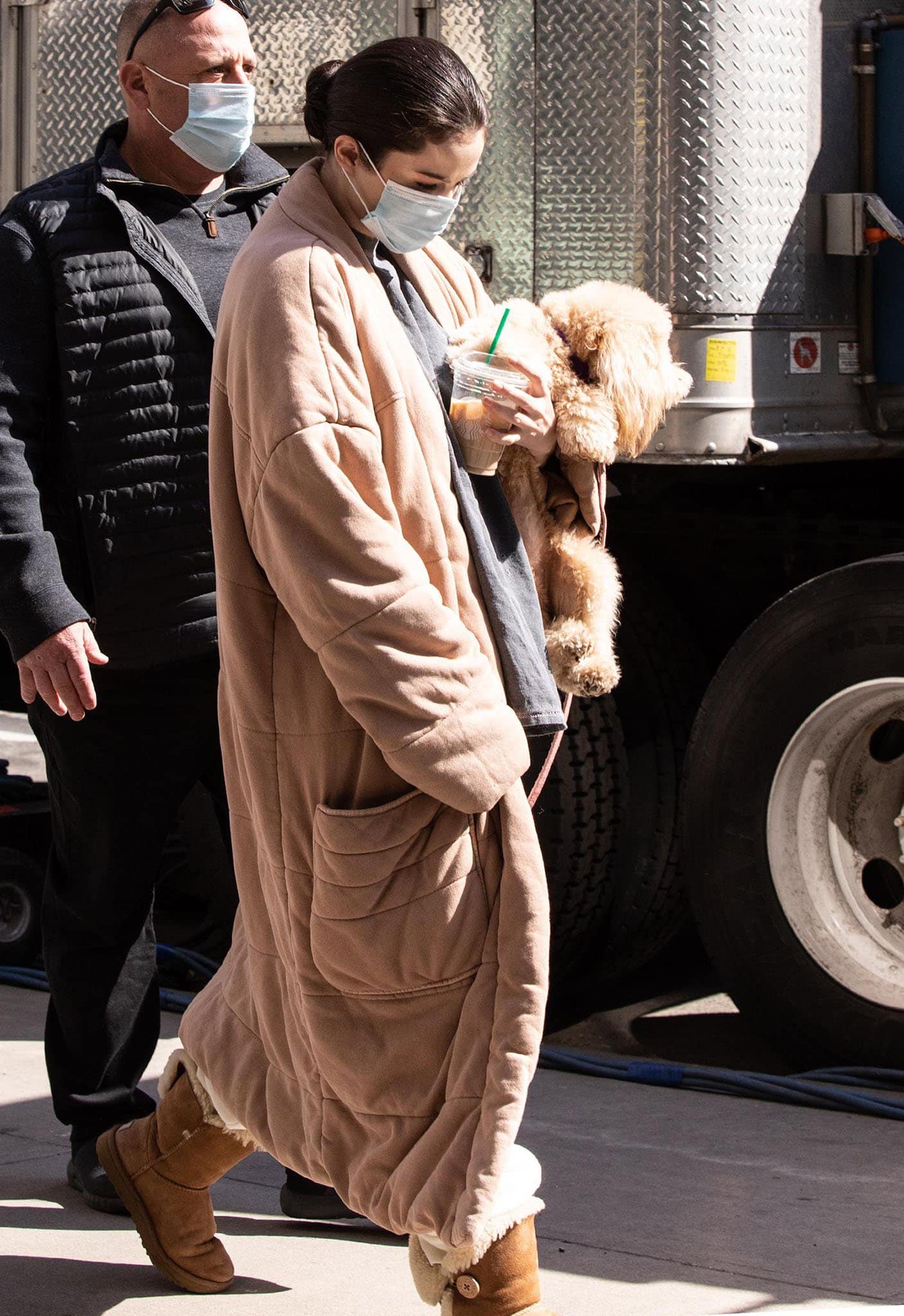 Selena Gomez keeps things cozy between takes, layering a Free People Dolman Duvet coat over her Revelación sweatpants and finishing the relaxed on-set look with classic UGG Bailey Button II boots while carrying her fluffy pup Daisy