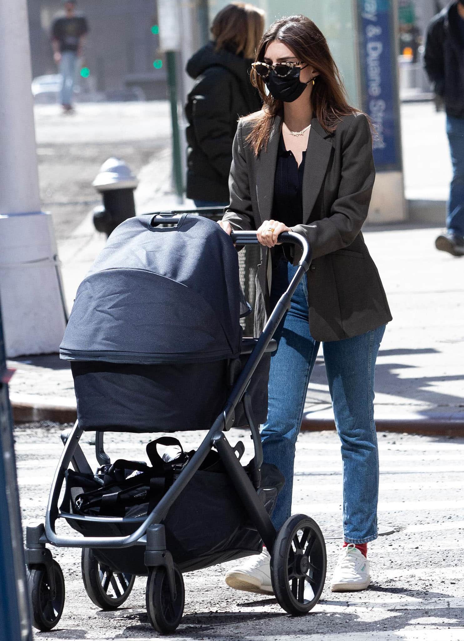 Emily Ratajkowski pairs straight-leg jeans and relaxed brown tailoring with white Reebok Club C 85 Vintage sneakers and bright red socks while pushing her son's stroller