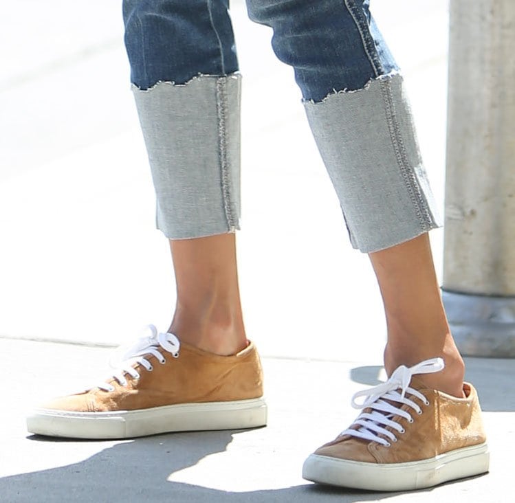 Alessandra Ambrosio pairs tan suede Common Projects Achilles sneakers with cuffed Mother jeans and a color-block knit sweater, blending relaxed denim with minimalist luxury footwear
