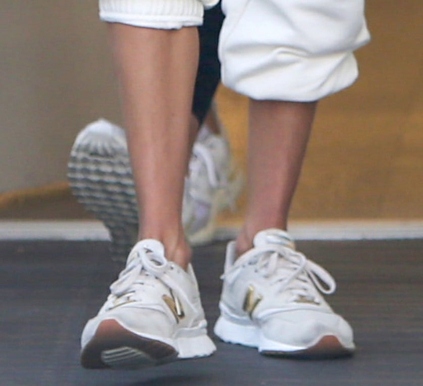 Alessandra Ambrosio pairs rolled white Alo sweatpants with gray-and-gold New Balance 997H sneakers, letting the retro-inspired runners add subtle contrast to her monochromatic athleisure look