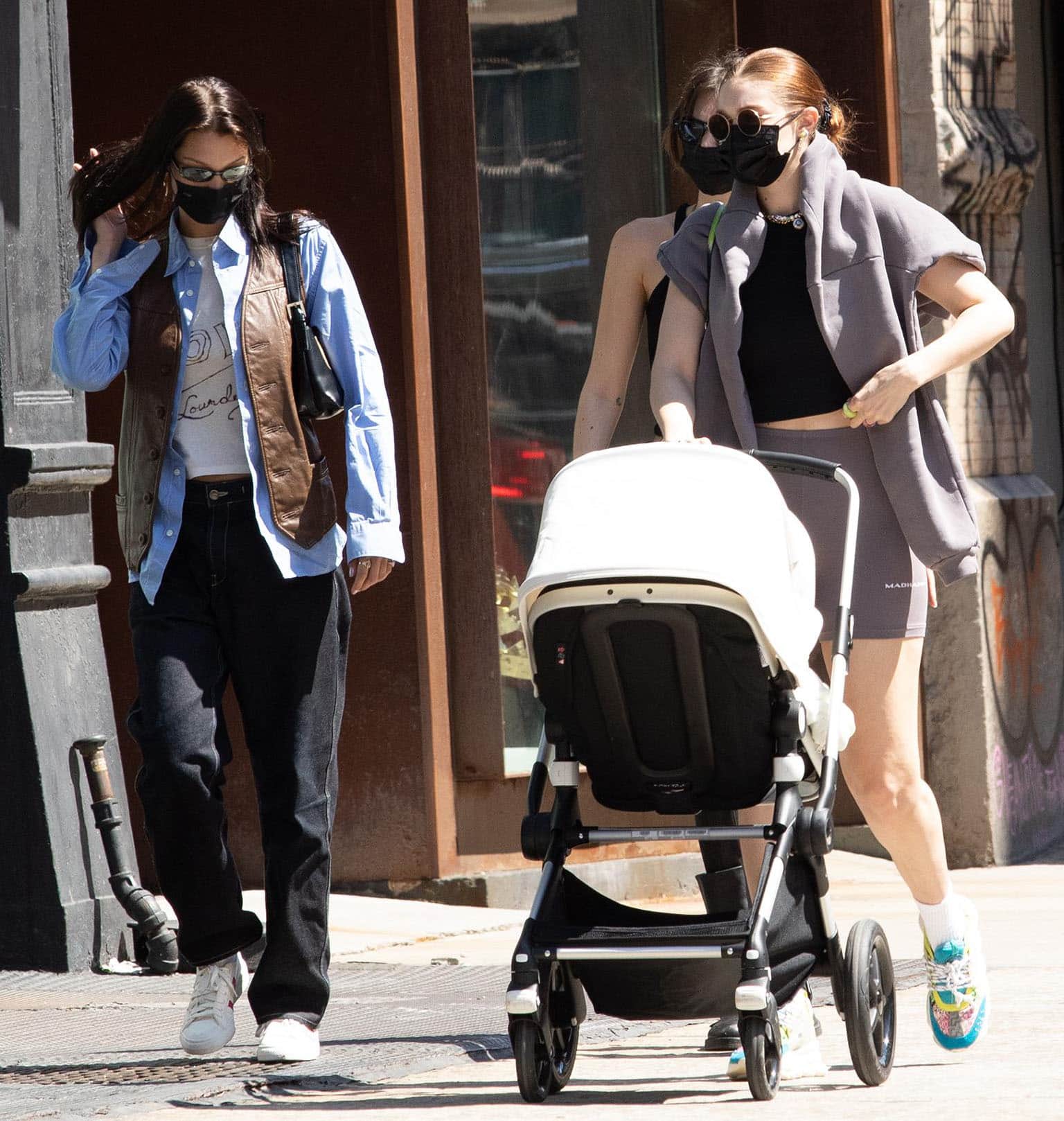 Gigi Hadid pushes daughter Khai in a Bugaboo Lynx stroller while wearing colorful Versace Chain Reaction sneakers as Bella Hadid follows in Adidas x Wales Bonner Nizza Lo sneakers