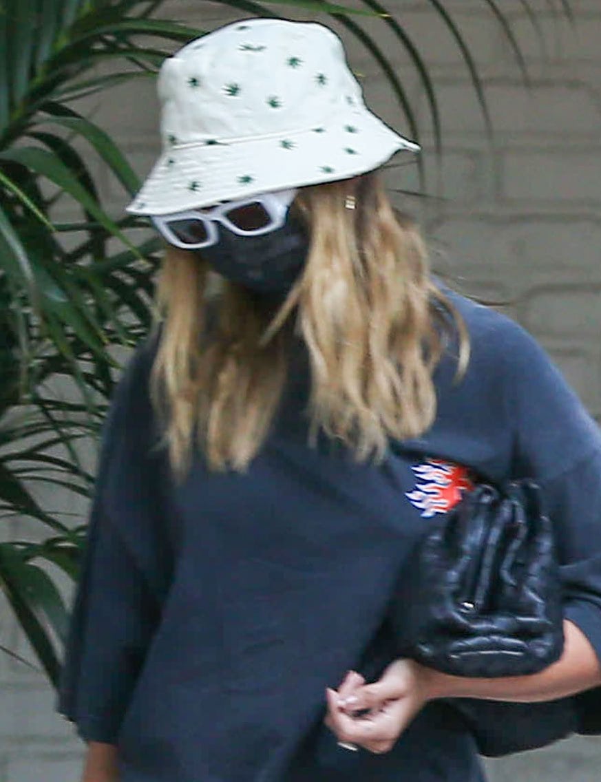 An embroidered Urban Outfitters bucket hat, Oscar and Frank white sunglasses, and Bottega Veneta’s black Pouch give Hailey Bieber’s casual look a designer finish