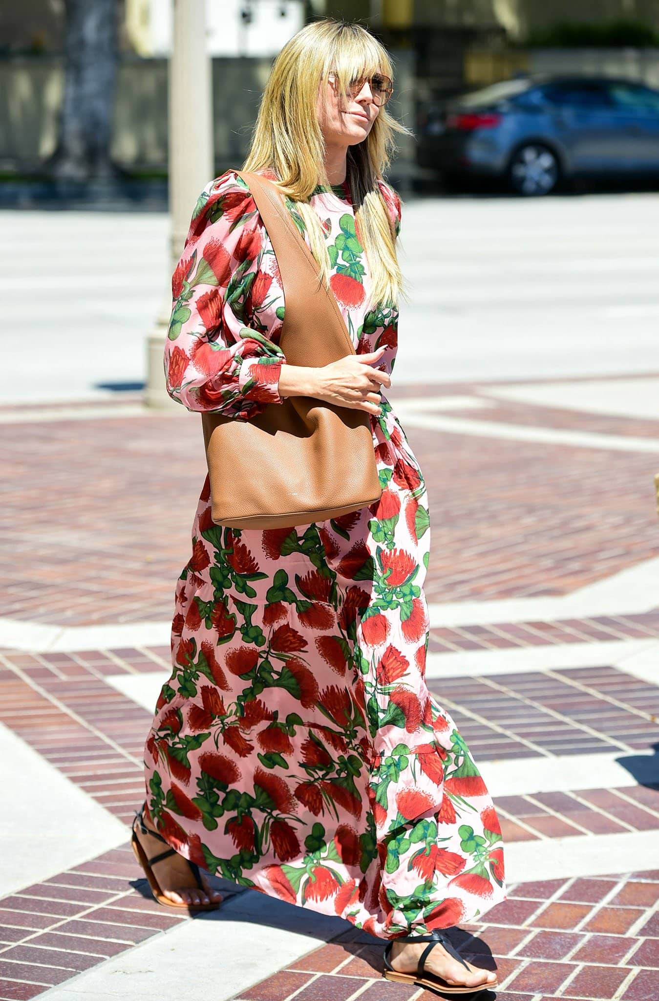 Heidi Klum embraces spring in a flowing Adriana Degreas floral dress, the soft pink base scattered with bold red blooms, styled with flat leather sandals and a slouchy tan tote for an easy, sunlit daytime look in Los Angeles on April 18, 2021
