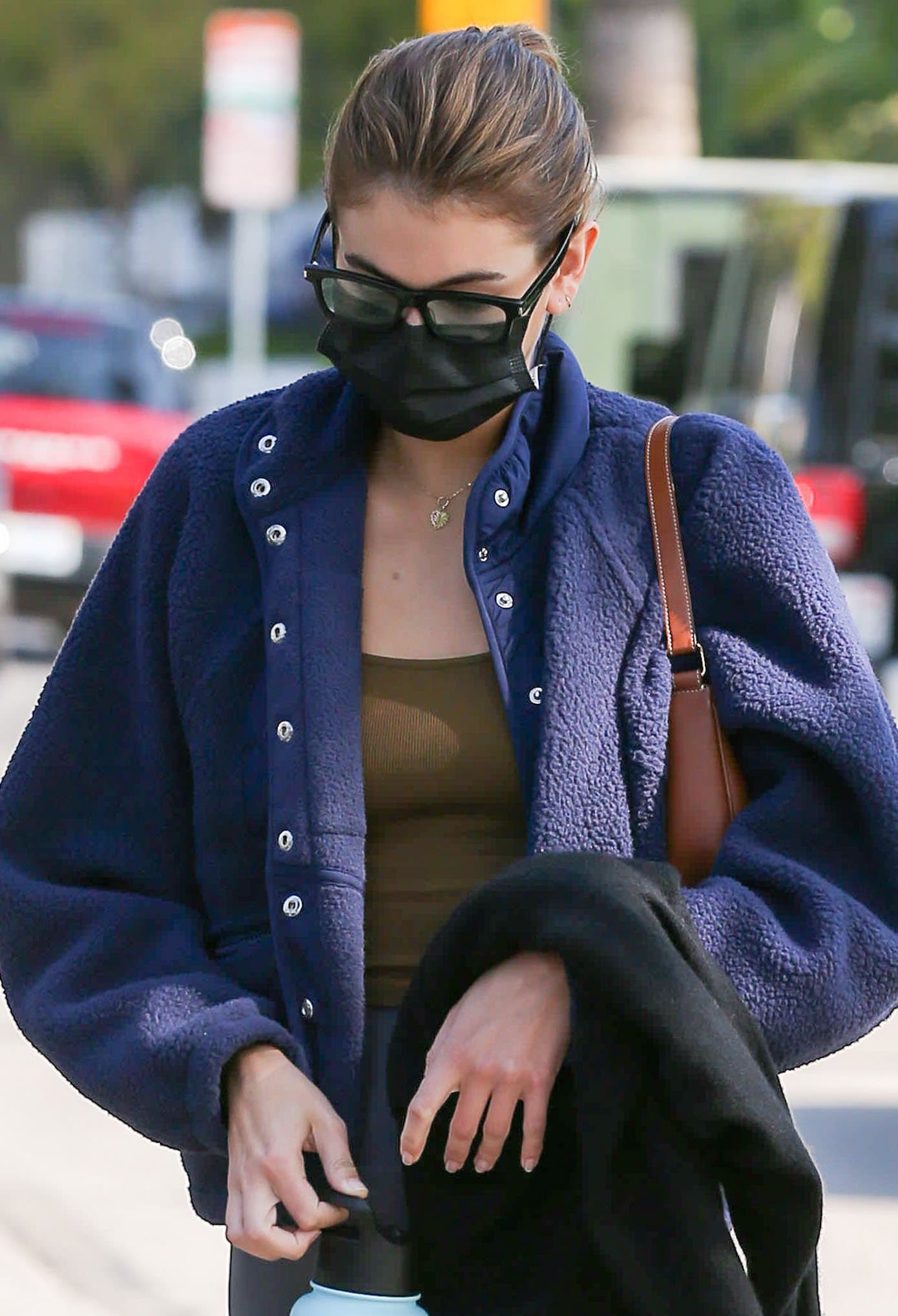 Kaia Gerber keeps her off-duty look grounded in cozy layers, pairing a textured fleece with sleek leggings while shielding her face behind angular glasses and a black mask
