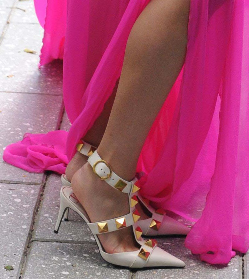 A close-up of Olivia Culpo’s white Valentino Garavani Roman Stud pumps reveals their pointed toes, caged T-straps, ankle straps, slim heels, and oversized gold pyramid studs