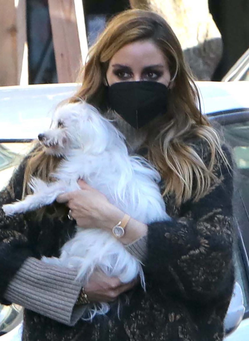 Olivia Palermo wears smoky eye makeup, loose waves, a black face mask, and a Piaget watch while holding Mr. Butler