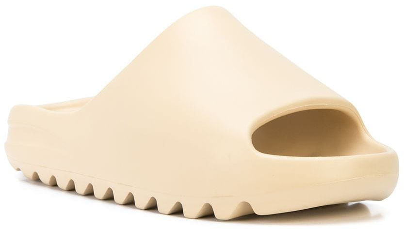 The Yeezy Slide in the Bone colorway features a sculptural one-piece EVA foam design with an open toe, cushioned footbed, and serrated outsole—delivering lightweight comfort and minimalist appeal that defined the slide’s rise in off-duty celebrity style