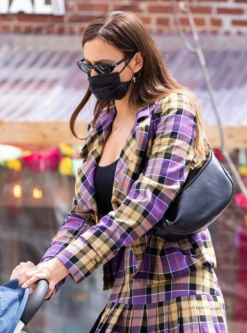 Irina Shayk elevates her Clueless-inspired plaid suit with edgy mismatched earrings, layered Jennifer Zeuner necklaces, and a sleek black By Far shoulder bag