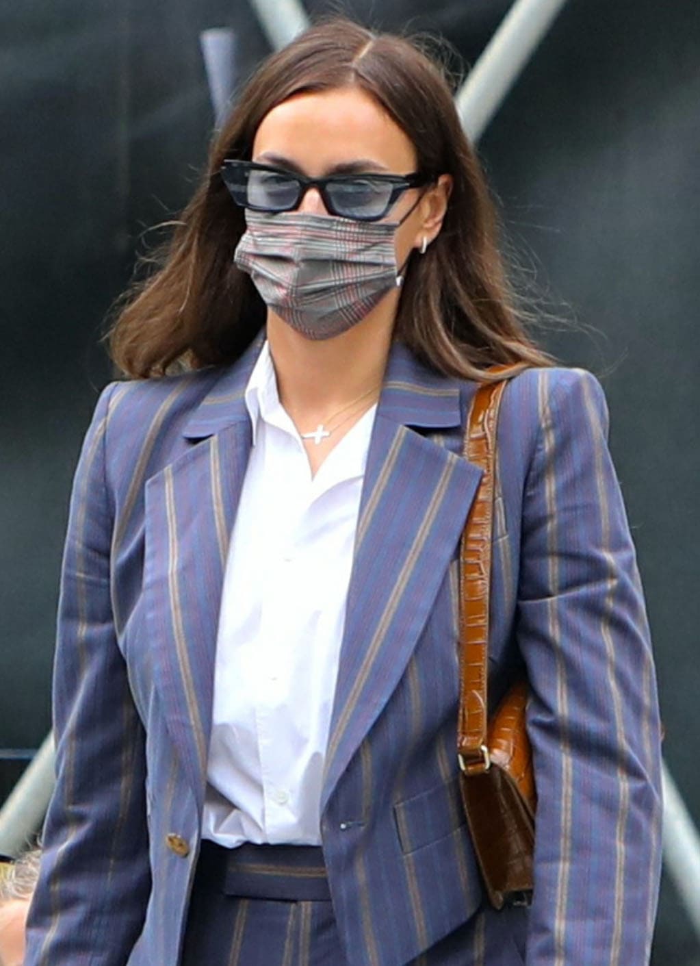 A closer look at Irina’s polished off-duty styling—sleek cat-eye sunglasses, a tartan mask, and a cross pendant offsetting structured suiting