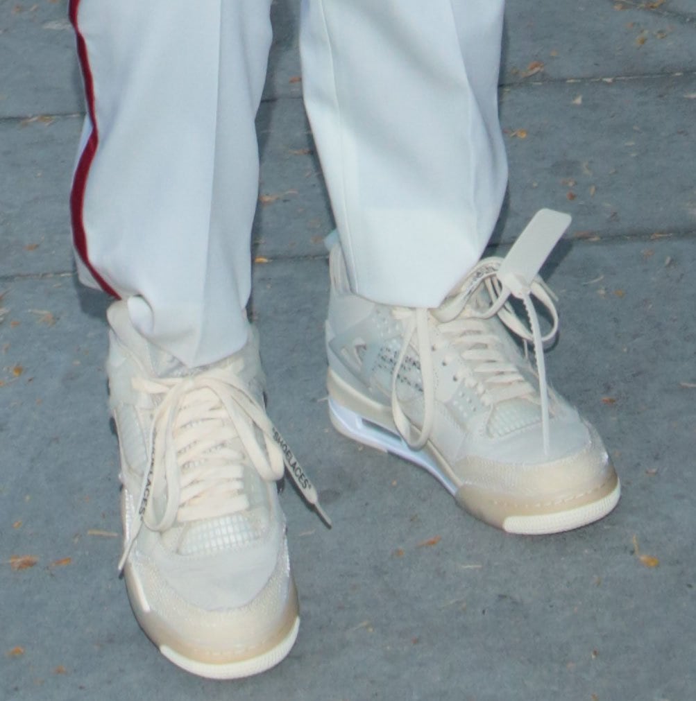 A close-up shows Kris Jenner’s Off-White x Air Jordan 4 “Sail” sneakers, including their translucent panels, exposed detailing, and signature zip tie